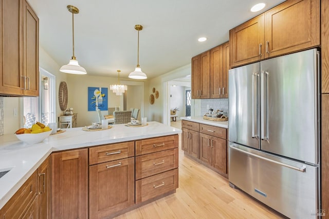 kitchen with high end fridge, brown cabinetry, light wood-style floors, and a peninsula