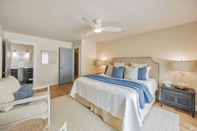 bedroom featuring baseboards, ensuite bath, light wood-type flooring, and a ceiling fan