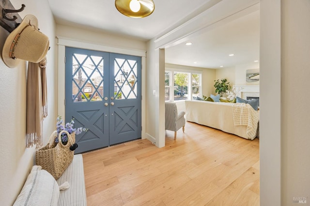 entrance foyer featuring a glass covered fireplace, recessed lighting, light wood-style flooring, and french doors