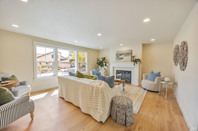 living room featuring recessed lighting, light wood-type flooring, a glass covered fireplace, and baseboards