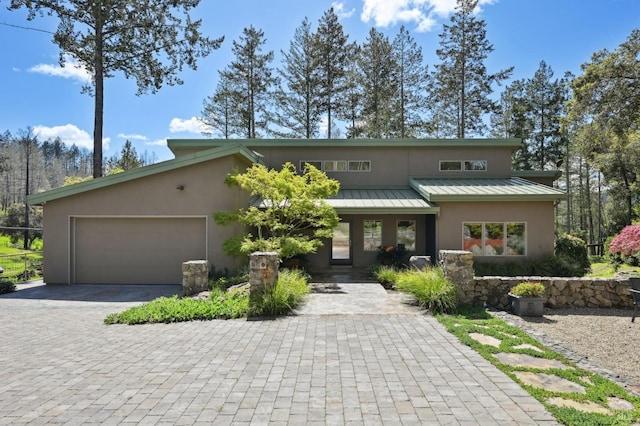 view of front facade with a standing seam roof, an attached garage, metal roof, stucco siding, and decorative driveway