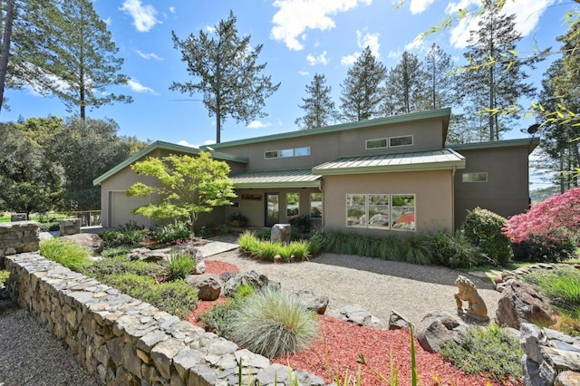 view of front of property with an attached garage, a standing seam roof, stucco siding, and metal roof