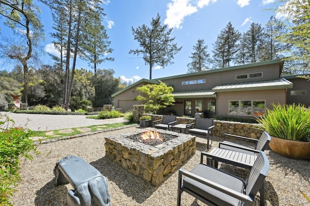 rear view of property with stucco siding, an attached garage, an outdoor fire pit, a standing seam roof, and metal roof