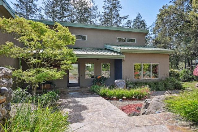 view of front facade with metal roof, a standing seam roof, and stucco siding
