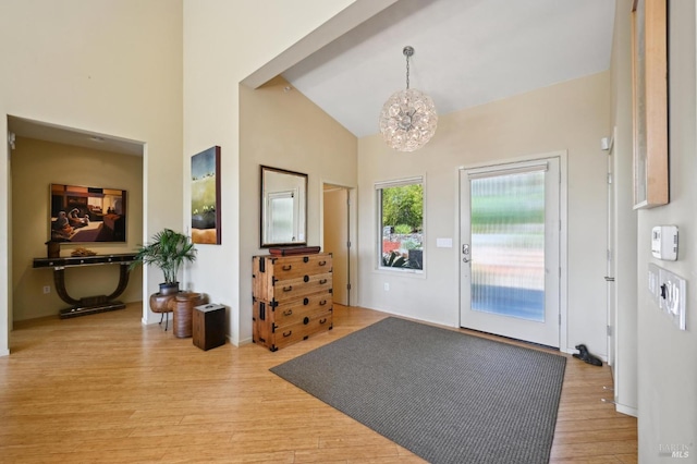 foyer with high vaulted ceiling, light wood-type flooring, and an inviting chandelier