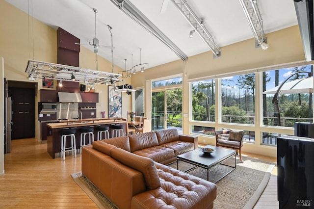 living room featuring light wood-style flooring, ceiling fan, and a high ceiling