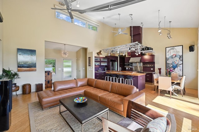 living area with a towering ceiling, light wood-style flooring, and ceiling fan