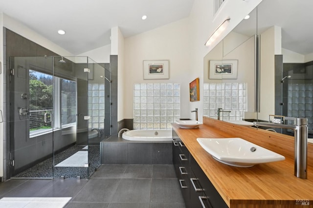 bathroom with a bath, double vanity, vaulted ceiling, tile patterned floors, and a stall shower