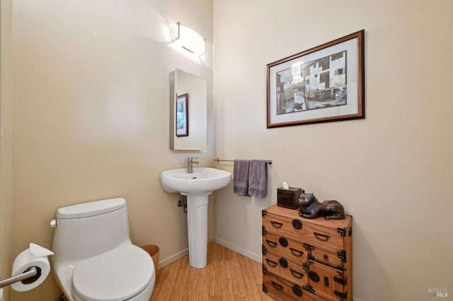 half bath with a sink, toilet, wood finished floors, and baseboards
