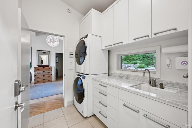 washroom featuring a chandelier, light tile patterned flooring, a sink, stacked washer and clothes dryer, and cabinet space