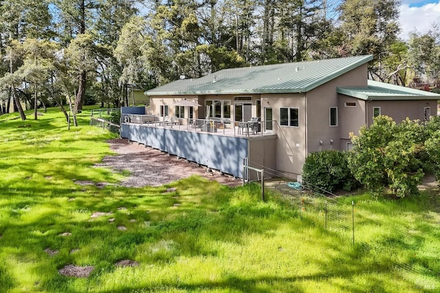 rear view of house featuring a standing seam roof, stucco siding, a lawn, metal roof, and fence