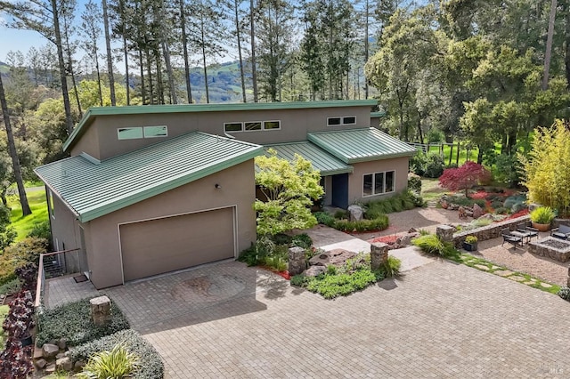 view of front of property with stucco siding, decorative driveway, a garage, a standing seam roof, and metal roof