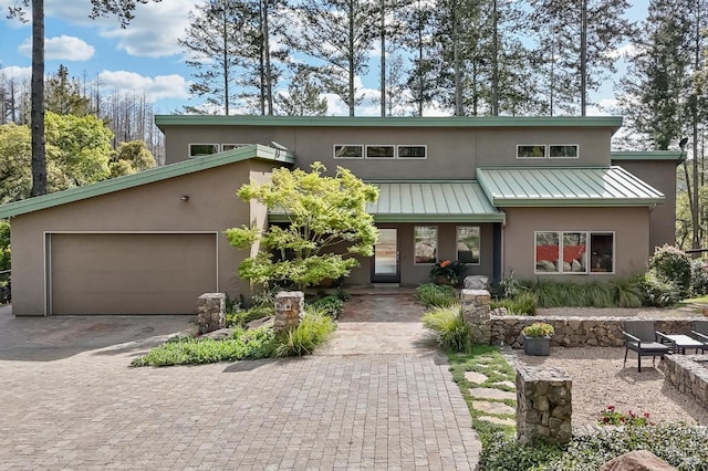 mid-century modern home with stucco siding, driveway, a garage, a standing seam roof, and metal roof
