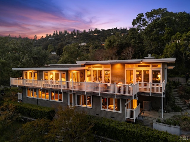 back of property at dusk with central AC unit and a wooded view