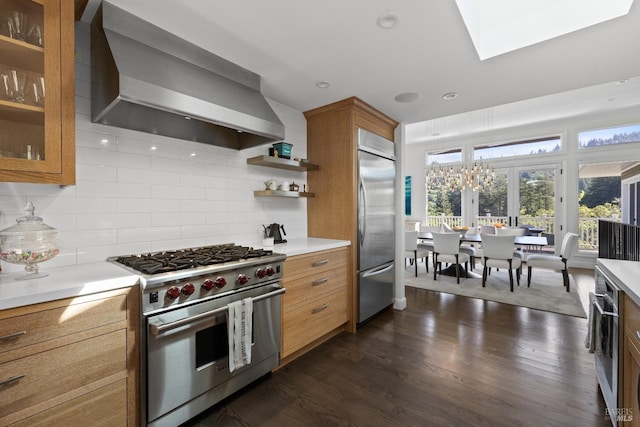kitchen featuring brown cabinetry, dark wood-style flooring, high quality appliances, light countertops, and wall chimney exhaust hood