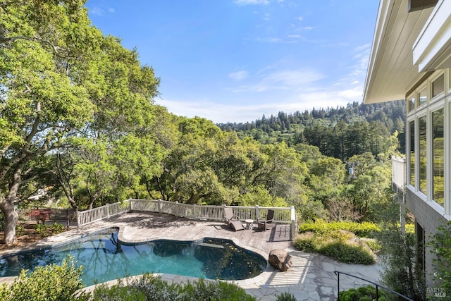 view of swimming pool with a patio, a fenced in pool, and a forest view