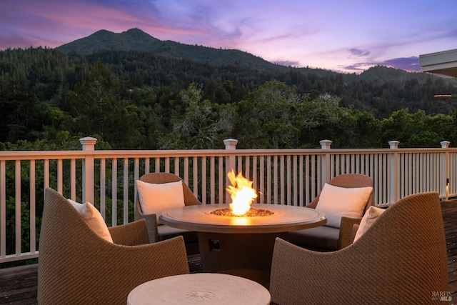 deck at dusk with a fire pit, a wooded view, and a mountain view