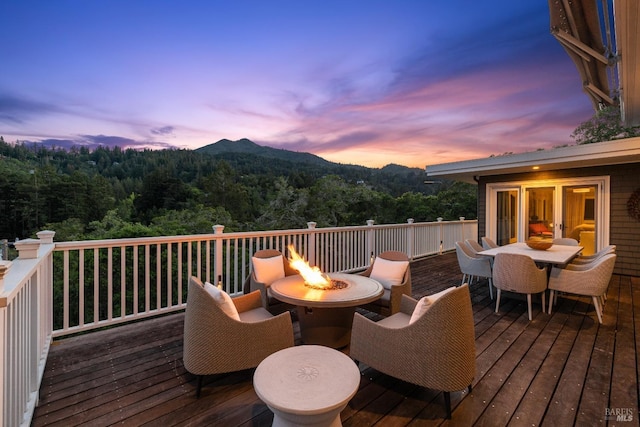 deck featuring a mountain view, a wooded view, outdoor dining space, and an outdoor fire pit