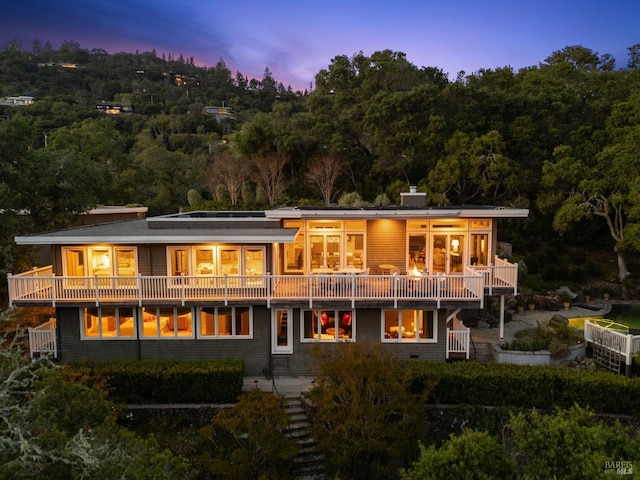 back of property at dusk with stairs, a view of trees, and a balcony