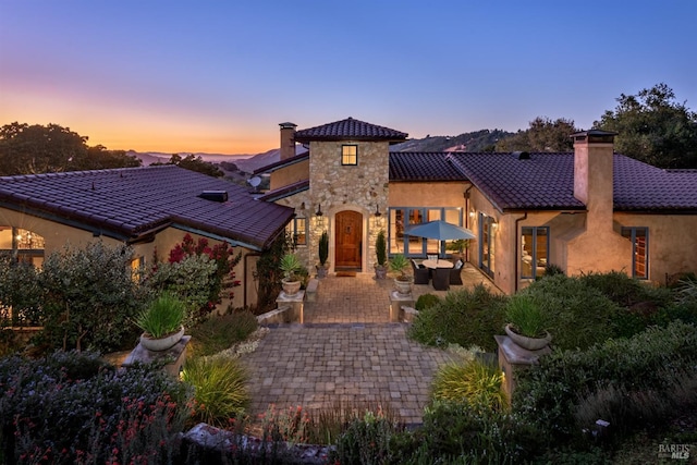 view of front of home featuring a chimney, a patio area, and a tile roof