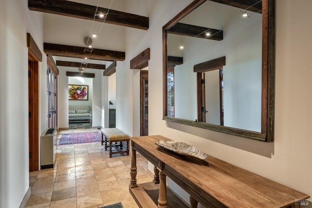 corridor with stone tile flooring, a healthy amount of sunlight, and beam ceiling