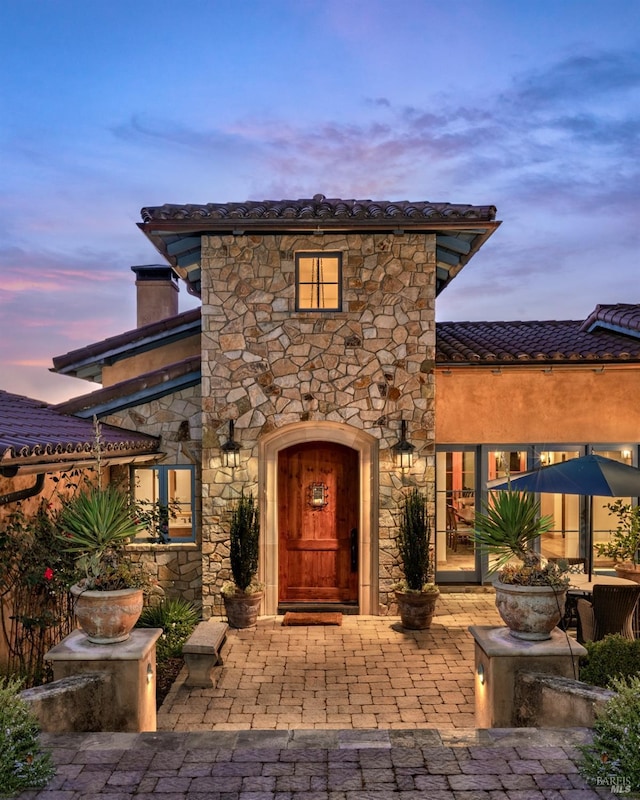 property entrance featuring stucco siding, stone siding, and a tile roof