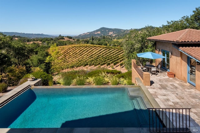 view of swimming pool with outdoor dining space, a mountain view, an infinity pool, and a patio area