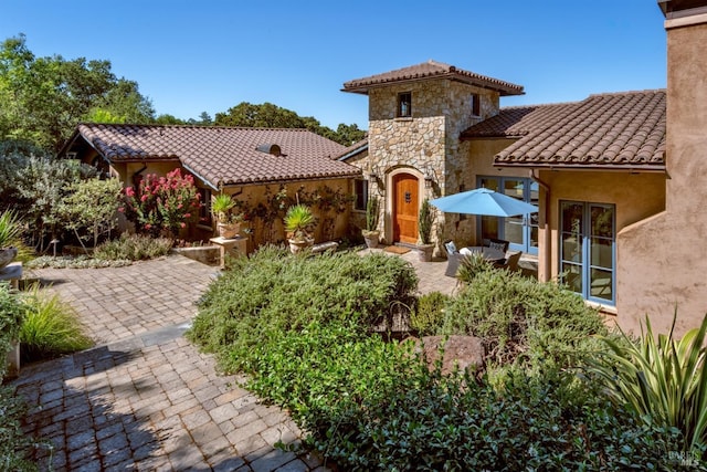 back of property with a patio, stucco siding, a tiled roof, and stone siding