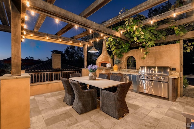 patio at night with area for grilling, a pergola, a grill, a sink, and outdoor dining area