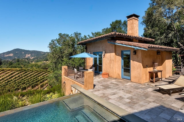 back of house featuring stucco siding, a patio, a tile roof, a chimney, and a mountain view