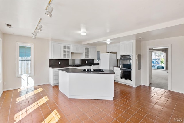 kitchen featuring tasteful backsplash, light tile patterned floors, a sink, dark countertops, and freestanding refrigerator