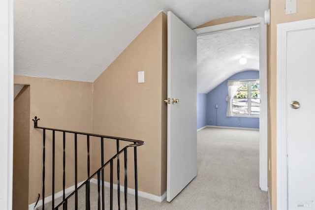 hallway with baseboards, carpet flooring, vaulted ceiling, and a textured ceiling
