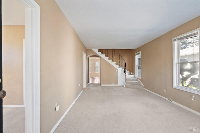 unfurnished living room with arched walkways, stairs, carpet floors, and a healthy amount of sunlight