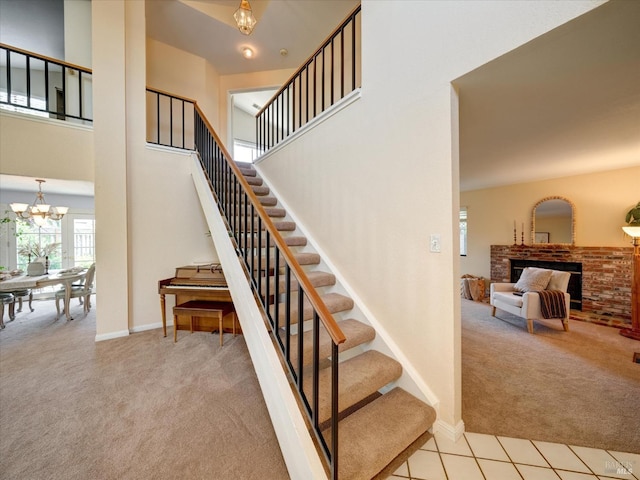 stairs with a towering ceiling, baseboards, an inviting chandelier, carpet flooring, and a brick fireplace