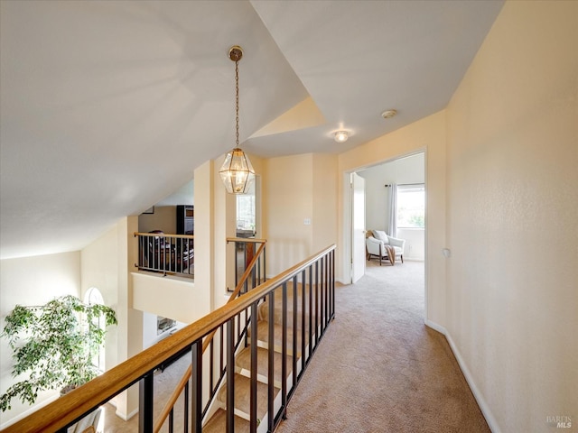 corridor with light carpet, an upstairs landing, baseboards, and vaulted ceiling