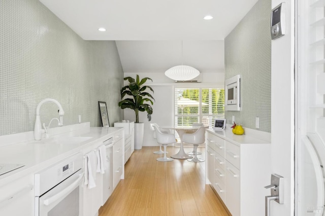 interior space featuring white oven, recessed lighting, a sink, decorative light fixtures, and light wood finished floors