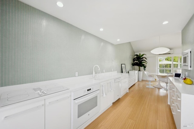 kitchen with a sink, light countertops, white appliances, light wood finished floors, and white cabinetry