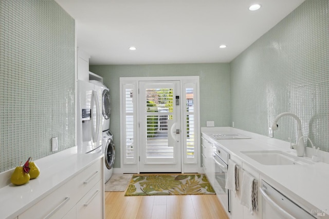 clothes washing area featuring stacked washer / dryer, light wood-style floors, a sink, and recessed lighting