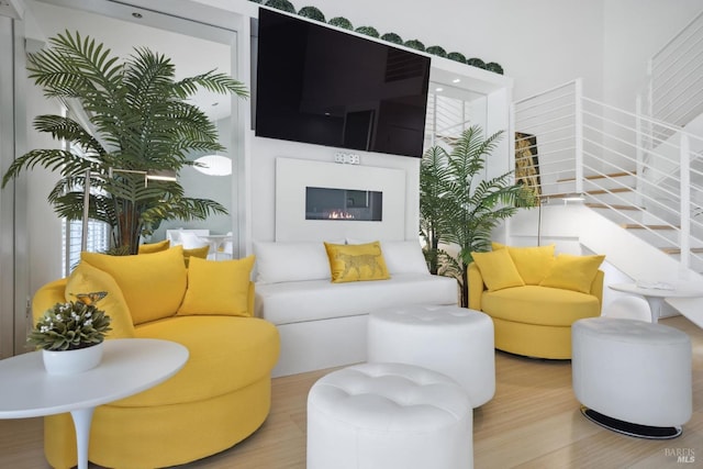 living room with a glass covered fireplace, wood finished floors, and stairs