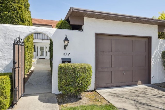 view of property exterior featuring french doors, concrete driveway, stucco siding, and a garage