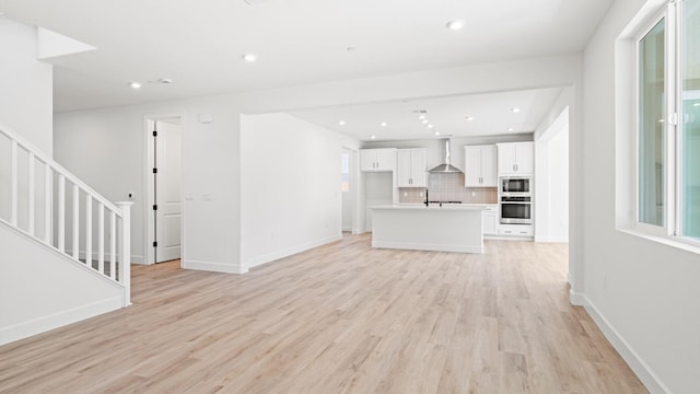 unfurnished living room featuring stairway, baseboards, a sink, light wood finished floors, and recessed lighting