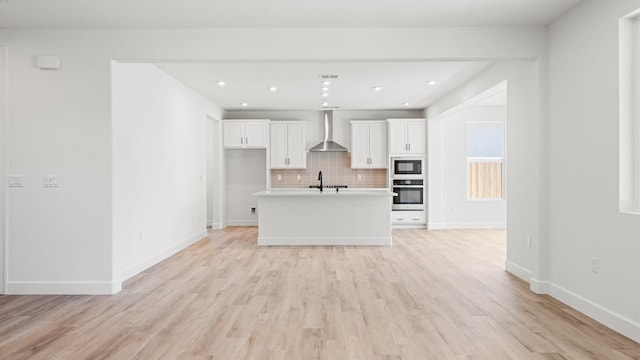 kitchen featuring black microwave, light wood-style floors, stainless steel oven, wall chimney range hood, and white cabinetry