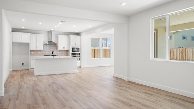 kitchen featuring wall chimney range hood, white cabinetry, open floor plan, and wall oven