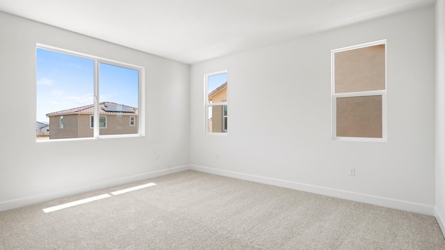 carpeted empty room featuring baseboards and plenty of natural light