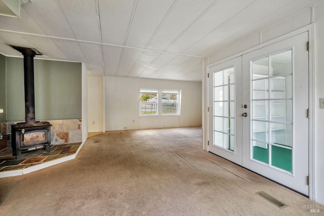 unfurnished living room featuring french doors, visible vents, carpet, and a wood stove