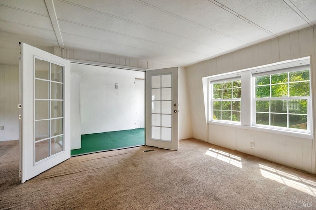 spare room with carpet floors, french doors, and wooden walls