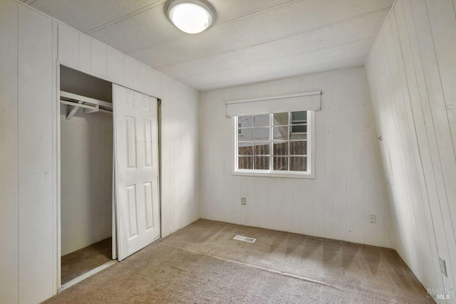 unfurnished bedroom with a closet, visible vents, carpet flooring, and wood walls