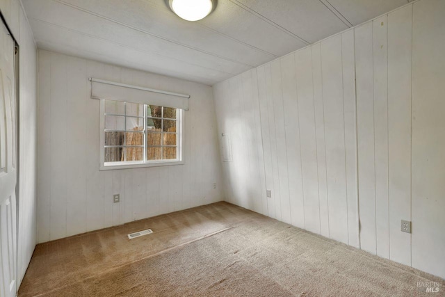 carpeted empty room featuring wooden walls and visible vents