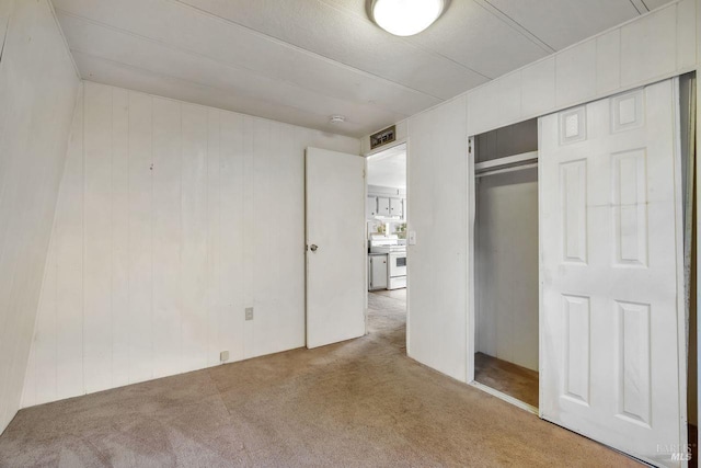 unfurnished bedroom with wood walls, a closet, and carpet
