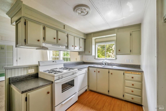 kitchen featuring under cabinet range hood, dark countertops, a sink, white appliances, and light wood-style flooring